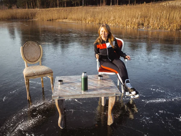 En flicka i skridskor sitter vid ett bord på en frusen sjö i skogen. Termos Tea Party — Stockfoto