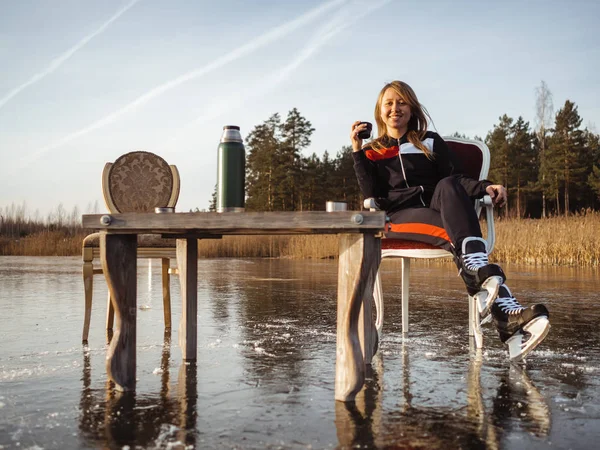 En flicka i skridskor sitter vid ett bord på en frusen sjö i skogen. Termos Tea Party — Stockfoto