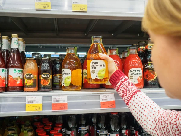 Bryansk, Rusia - 20 de diciembre de 2019: Chica elige una bebida. Escaparate con botellas de jugo en la tienda Lenta —  Fotos de Stock