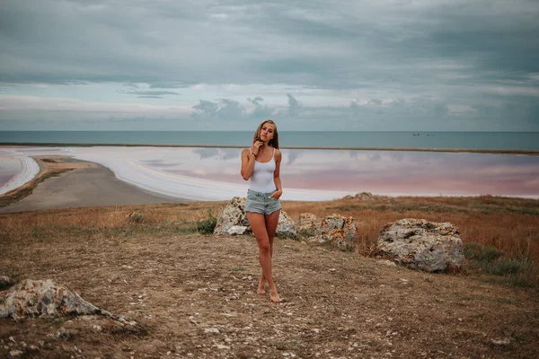 Retrato completo de una chica en pantalones cortos y un body blanco en el fondo de un lago rosa salado — Foto de Stock