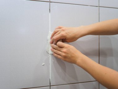 Banyodaki fayanslar arasında sayıyorum. Kadın eli bir spatula tutuyor. Onarım.