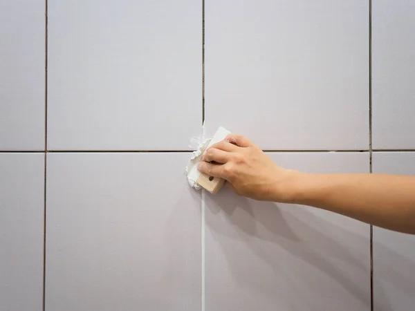 Banyodaki fayanslar arasında sayıyorum. Kadın eli bir spatula tutuyor. Onarım.