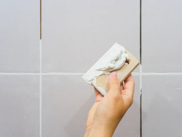Banyodaki fayanslar arasında sayıyorum. Kadın eli bir spatula tutuyor. Onarım.