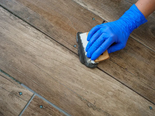 Grouting between ceramic tiles. A hand in a blue glove holds a spatula. Repair in the room.