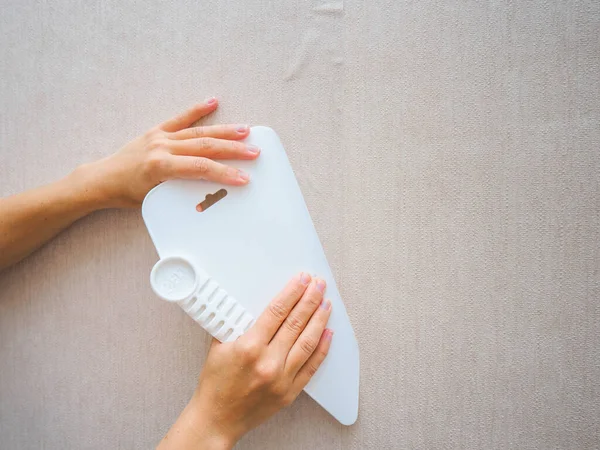 Apartmanda tamirat var. Kız işçi, duvar kağıdının yapıştırıcı şeridini bir spatulayla yumuşatıyor. Yeni ev partisi..
