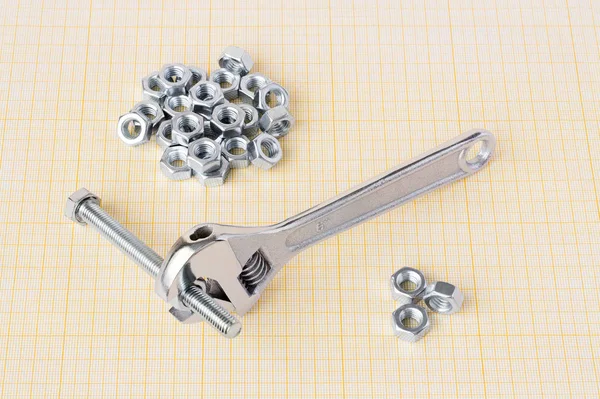 Spanner, bolt and nuts on graph paper — Stock Photo, Image