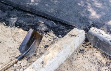 Yaya yolu yeni asfaltla kaplı. Kürek ve kaldırım taşları yerde yatıyorlar. Yolların onarımı