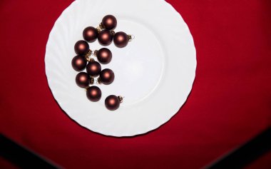 Kırmızı masada yeni yıl oyuncakları olan beyaz tabak.