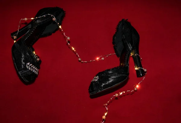 Black shoes with fringe and rhinestones lie on a red background