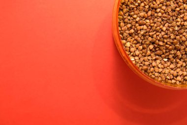 Köşedeki kırmızı arka planda plastik bir kabın içinde pişmemiş karabuğday.