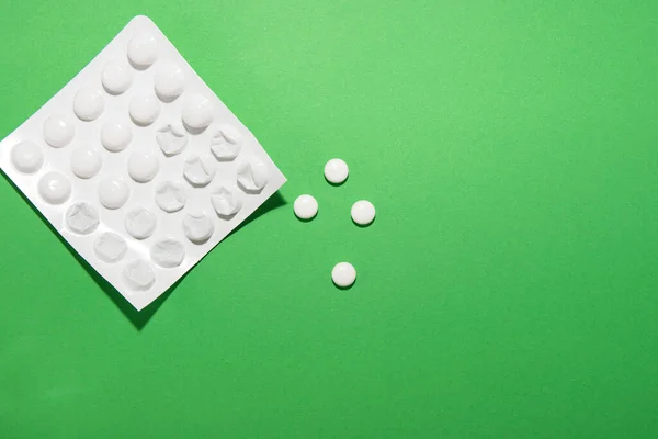Half-used medicine packaging lie on a green background, several tablets fell out
