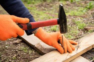 Turuncu eldivenli eller kırmızı saplı bir çiviyi kırmızı saplı bir tahtaya çakıyor.