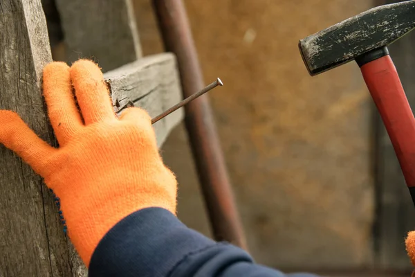 Hand in orange gloves hammer a nail with a red handle