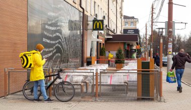 Tula, Rusya, 21 Nisan 2020. Kapalı karantina McDonald 's restoranı ve kuryesi sarı ve bisikletli ve yoldan geçenler