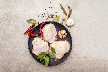 Çiğ tavuk budu ve baharat. Taş zeminde et pişirmek için gerekli malzemeler. Sıcak ve karabiber, sarımsak, biberiye, defne yaprağı, üst manzara..