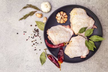Çiğ tavuk budu ve baharat. Taş zeminde et pişirmek için gerekli malzemeler. Acı ve karabiber, sarımsak, biberiye, defne yaprağı, üst manzara, kapat.