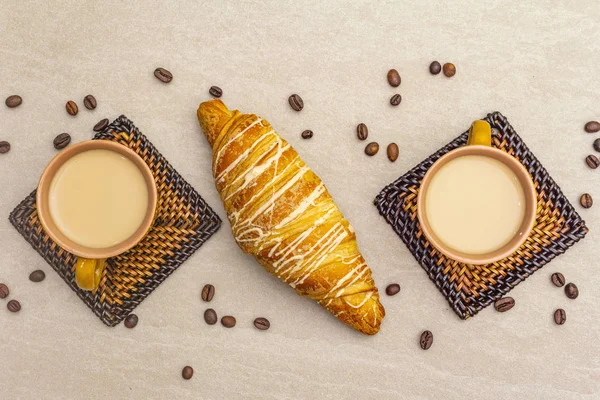 Une tasse de café frais avec croissant. Le concept sur un fond de pierre avec des grains de café torréfiés et des dessous de verre en osier, vue de dessus, gros plan . — Photo