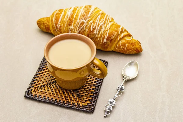 Une tasse de café frais avec croissant. Le concept sur fond de pierre avec dessous de verre en osier et cuillère vintage en argent, gros plan . — Photo