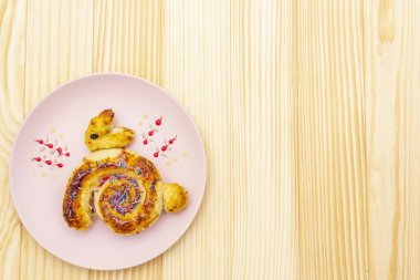 Paskalya tavşanı şeklinde taze çörek. Çocukların bayram yemeği konsepti. Ahşap zemin üzerinde pembe seramik plaka, kopyalama alanı, üst görünüm.