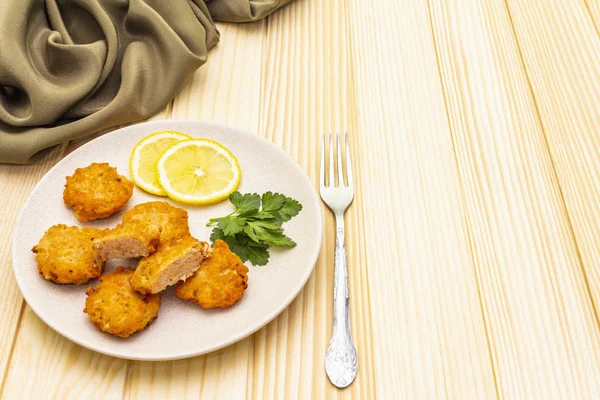 Homemade red fish cakes with lemon and parsley in ceramic plate. With fabric drapery and fork on wooden background, copy space.