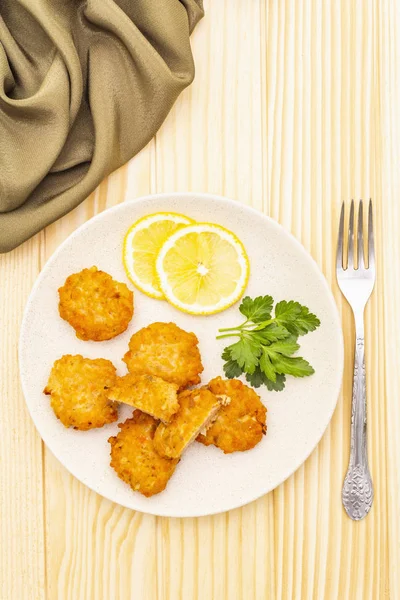Homemade red fish cakes with lemon and parsley in ceramic plate. With fabric drapery and fork on wooden background, top view.