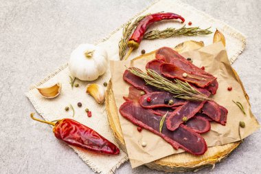 Basturma, kurutulmuş sığır filetosu, kurutulmuş et, ince dilimlenmiş. Kuru biberiye, biber karışımı, kırmızı biber, kaliteli keten kumaşlı sarımsak. Tahtadaki lezzetli yemekler, taş arka plan, kapat..