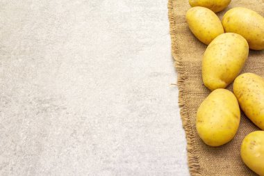 Çuval bezinde soyulmamış genç patatesler. Yeni hasat, taş zeminde yığın, üst görünüm, kopyalama alanı.