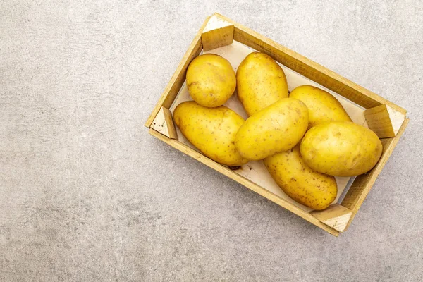 Batatas jovens cruas não descascadas em uma caixa de madeira. Nova colheita, no fundo de pedra, espaço de cópia, vista superior — Fotografia de Stock