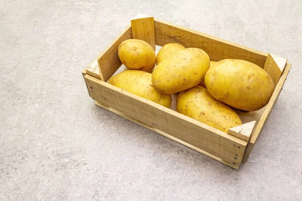 Batatas jovens cruas não descascadas em uma caixa de madeira. Nova colheita, no fundo de pedra, espaço de cópia — Fotografia de Stock