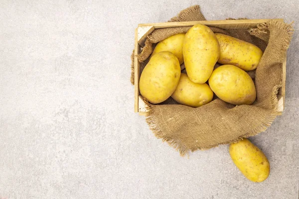 Raw unpeeled young potatoes in a wooden crate. New harvest, on sackcloth, stone background, copy space, top view. — 스톡 사진