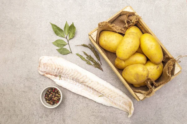 Petites pommes de terre crues et filets de merlu congelés. Ingrédients pour fish and chips. Épices et herbes sur fond de pierre, gros plan, vue sur le dessus . — Photo