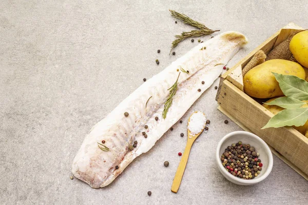 Rauwe jonge aardappelen en bevroren heekfilets. Ingrediënten voor fish and chips. Specerijen en kruiden op een stenen achtergrond, kopieerruimte, close-up. — Stockfoto