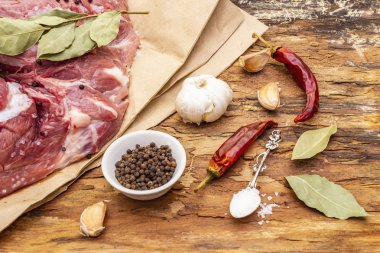 Çiğ domuz omuzu ve baharat. Koyun yaprağı, sarımsak, kırmızı biber. Ahşap bir arka planda, yakın plan.