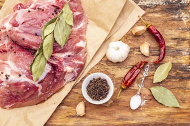 Çiğ domuz omuzu ve baharat. Koyun yaprağı, sarımsak, kırmızı biber. Ahşap bir arka planda, yakın plan, üst manzara.