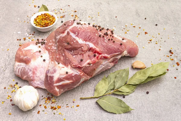 Raw pork shoulder with spices. Bay leaf, garlic. On a stone background, close up.