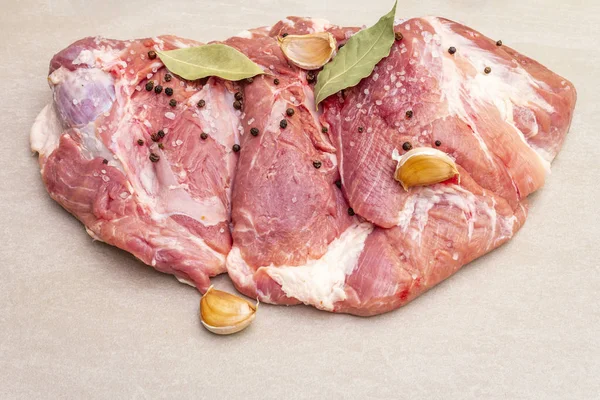 Raw pork shoulder with spices. Bay leaf, garlic. On a stone background, copy space, close up.