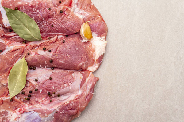 Сырое свиное плечо со специями. Лист лавровый, чеснок. На каменном фоне, скопировать пространство, вид сверху, закрыть
.