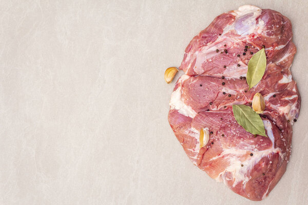 Сырое свиное плечо со специями. Лист лавровый, чеснок. На каменном фоне, пространство для копирования, вид сверху
.