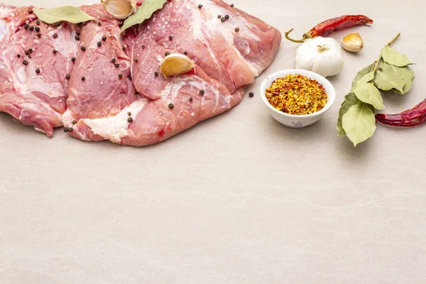 Raw pork shoulder with spices. Bay leaf, garlic. On a stone background, copy space.