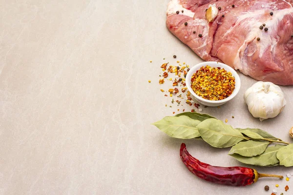 Raw pork shoulder with spices. Bay leaf, garlic. On a stone background, copy space.