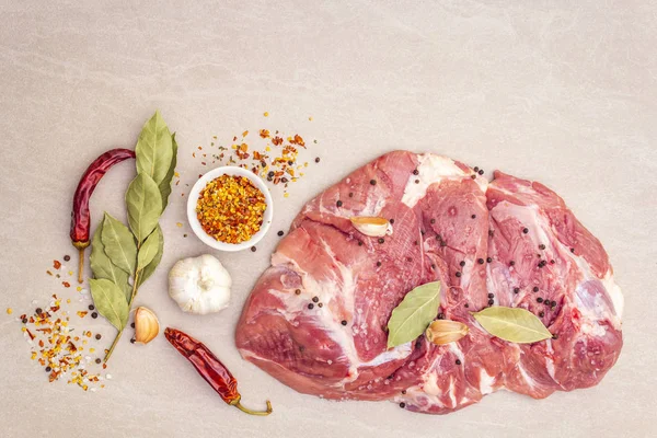 Raw pork shoulder with spices. Bay leaf, garlic. On a stone background, close up, top view.