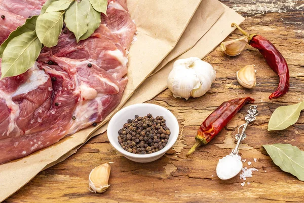 Raw pork shoulder with spices. Bay leaf, garlic, chili. On a wooden bark background, close up.