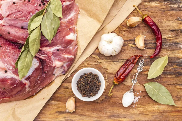 Raw pork shoulder with spices. Bay leaf, garlic, chili. On a wooden bark background, close up, top view.