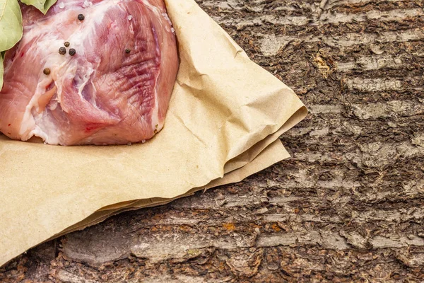 Raw pork shoulder with black pepper. On a wooden bark background, close up, copy space