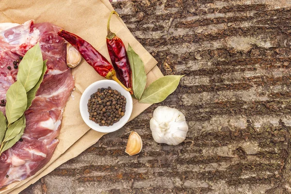 Raw pork shoulder with spices. Bay leaf, garlic, chili. On a wooden bark background, close up, top view, copy space. — Stock Photo, Image