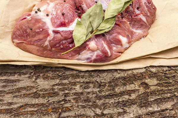 Raw pork shoulder with black pepper and bay leaf. On a wooden bark background, close up, copy space