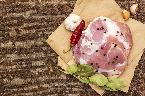 Hombro de cerdo crudo con especias. Hoja de laurel, ajo, chile. Sobre un fondo de corteza de madera, vista superior, espacio para copiar . — Foto de Stock