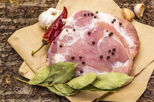 Hombro de cerdo crudo con especias. Hoja de laurel, ajo, chile. Sobre un fondo de corteza de madera, de cerca . — Foto de Stock