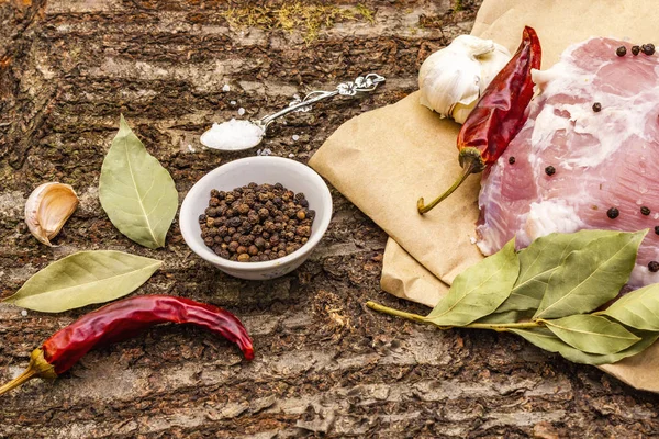 Raw pork shoulder with spices. Bay leaf, garlic, chili. On a wooden bark background, close up.