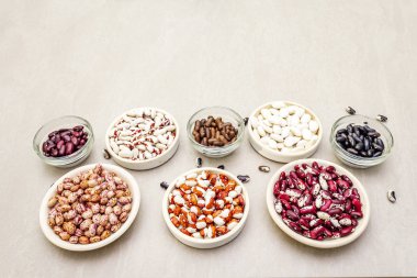 Assortment of beans on a stone background. Crimson cranberry, red, painted pony, black turtle, brown, black-eyed, Jacob's Cattle (heirloom) and lima. clipart